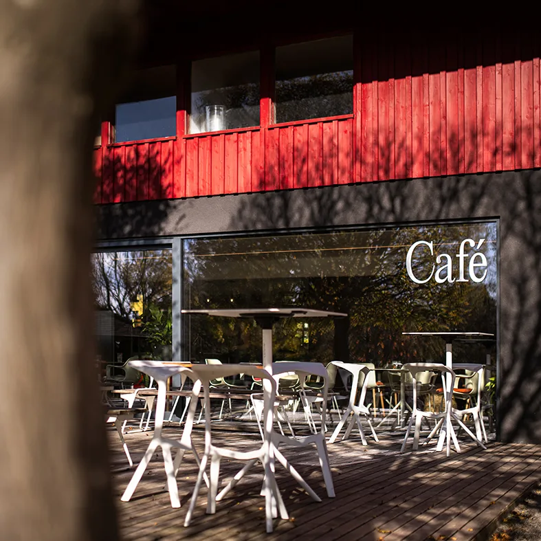 Eingang des Garten Cafés mit Schriftzug Café und weißen Stühlen auf der Holzterrasse