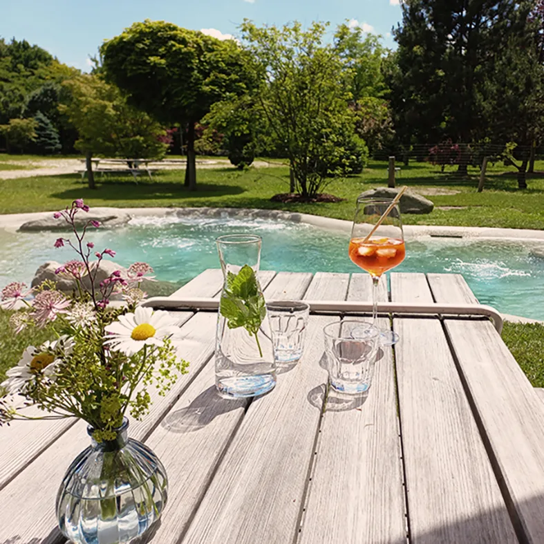 Holztisch mit Blumen und Getränk am BioDesign-Showpool im Baumpark