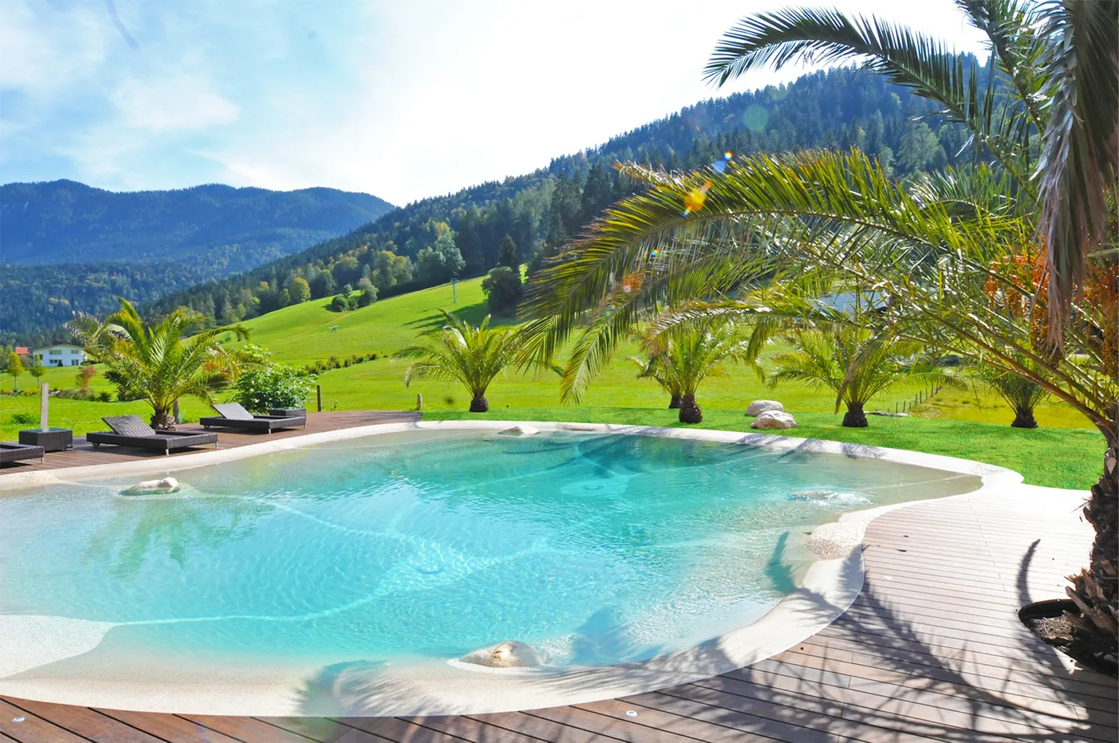 Biodesign-Pool mit Strandzone, Holzdeck und Palmen vor einer Berglandschaft