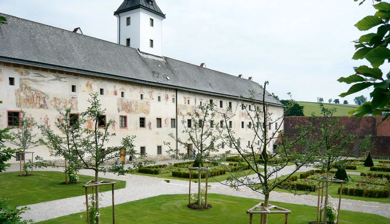 Renaissancepark mit jungen Bäumen und Buchsbeeten vor einem historischen Gebäude mit Turm