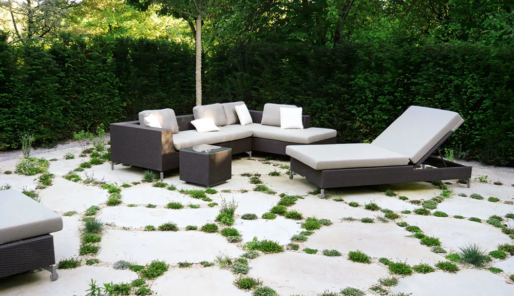 Terrasse aus großen Natursteinplatten mit begrünten Fugen und Loungemöbeln