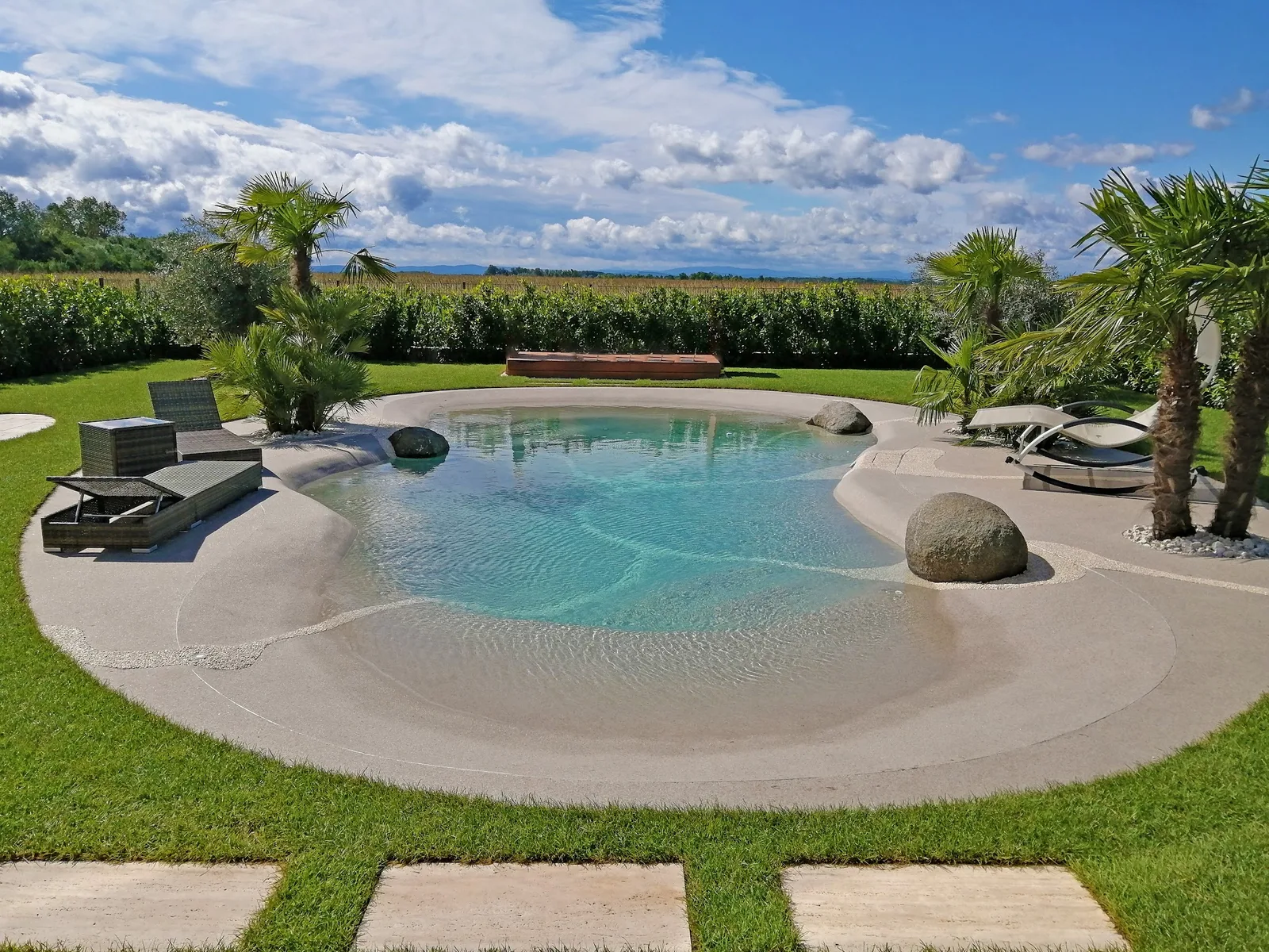 Biodesign-Pool mit Strandeinstieg, Palmen und Trittplatten im Rasen