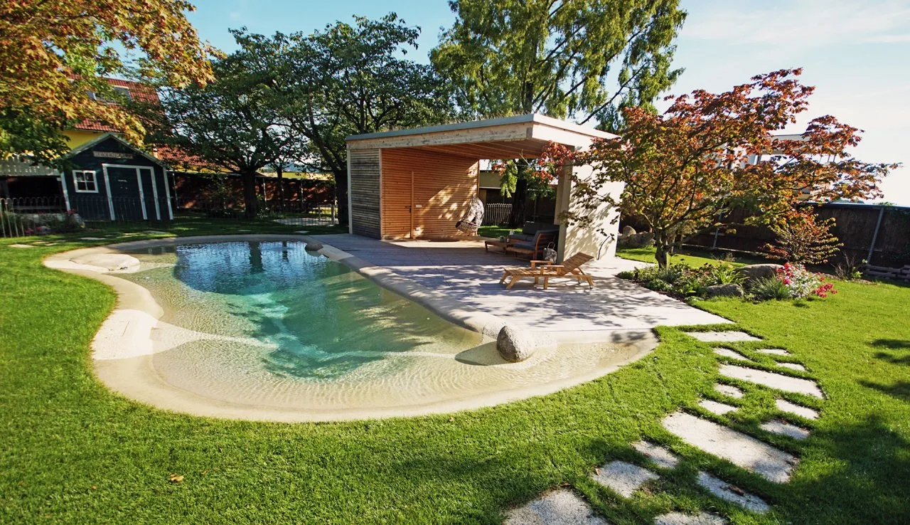 Biodesign-Pool mit Strandzone, Holzpavillon und Trittplatten im Rasen