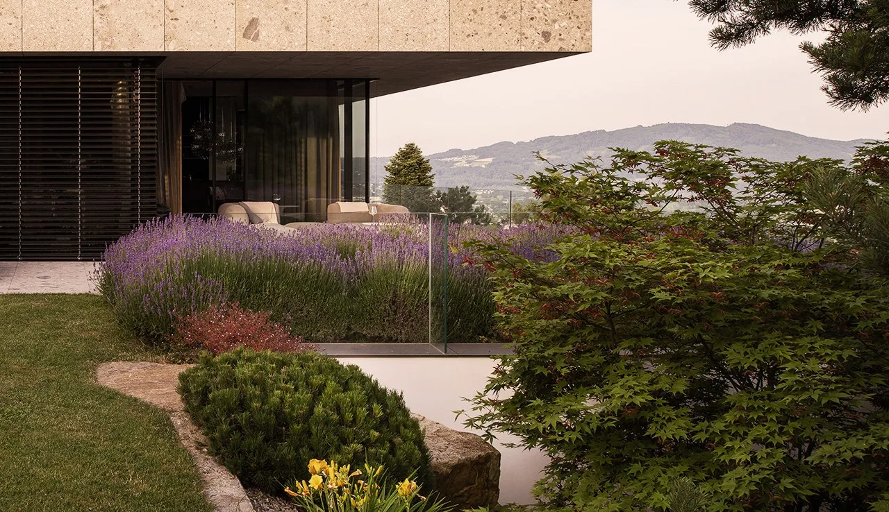 Villengarten mit Lavendel, Kiefern und Findlingen vor einem Haus aus Naturstein